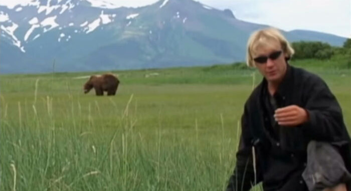 Man in a field with a bear in the background, wearing sunglasses, highlighting a creepy photo with a dark history.