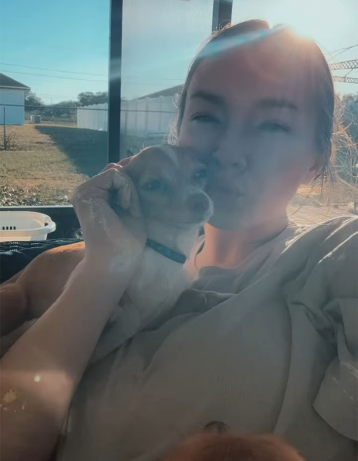 Influencer with her dog in a sunlit area, holding the pet close, smiling softly at the camera.