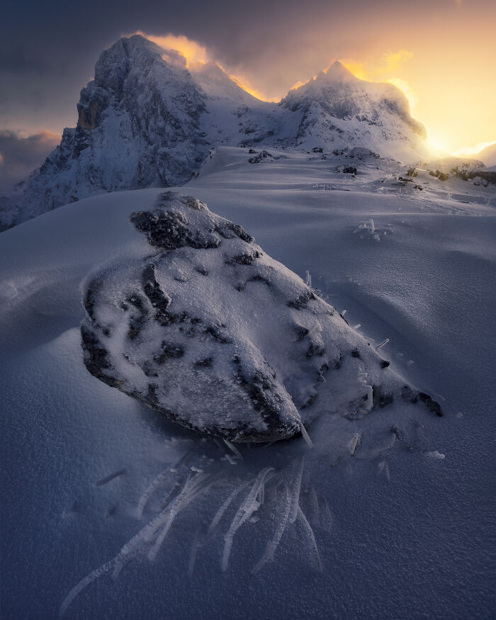 Snow-covered mountain landscape at sunrise, showcasing a stunning view of snow and rock formations against a glowing sky.
