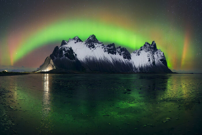 Stunning landscape with green aurora over snowy mountains reflecting in icy water.