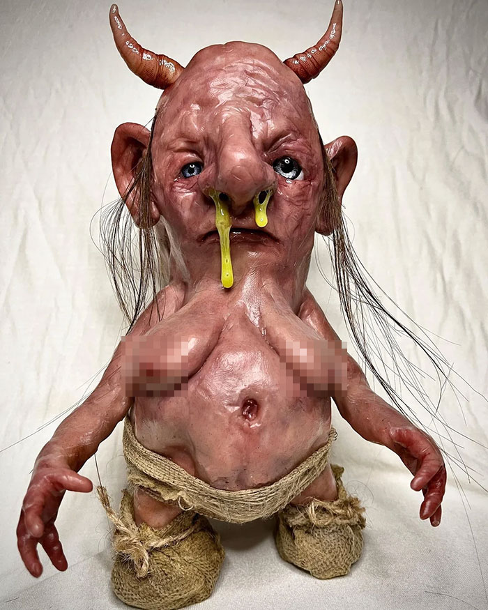 Creepy handmade craft of a small creature with horns, yellow eyes, and rough fabric clothing.