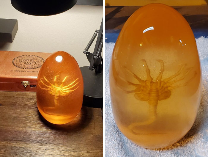 Creepy handmade craft in resin featuring a creature encased, placed on a wooden table under a lamp.