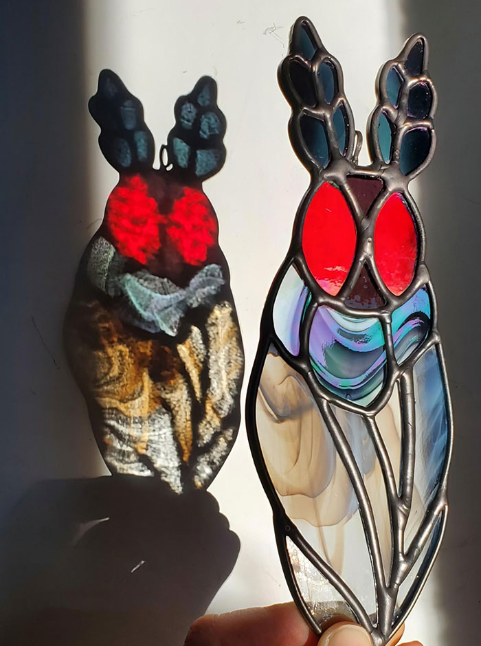 Stained glass cicada with vibrant red eyes casting an intricate shadow, showcasing interesting creepy handmade crafts.