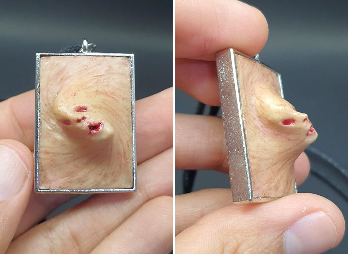 Creepy handmade craft pendant with distorted face design, held between fingers.