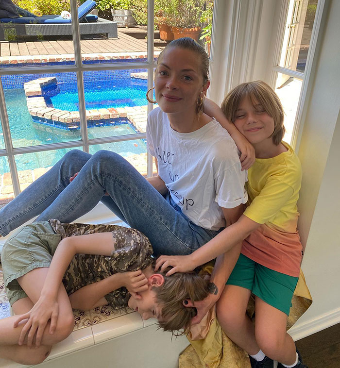 Jaime King sitting with two children by a window, a pool visible outside. Jaime King sitting with two children by a window, a pool visible outside.