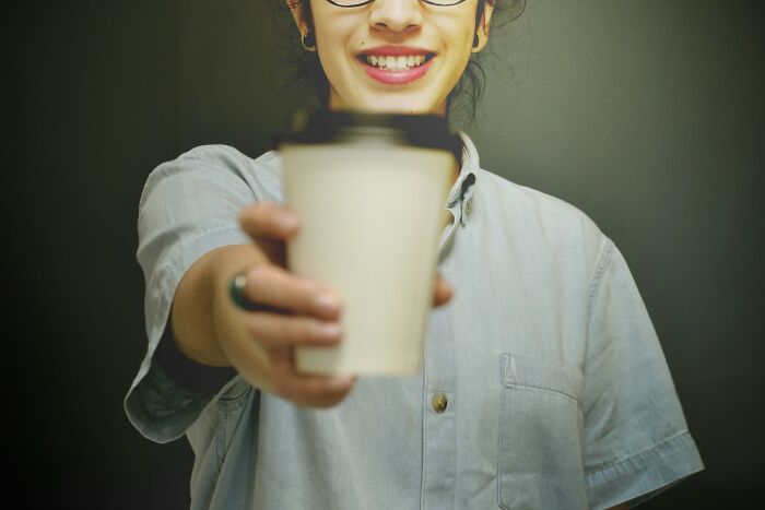 A person smiling and offering a takeaway coffee cup, representing a worst job bonus scenario.