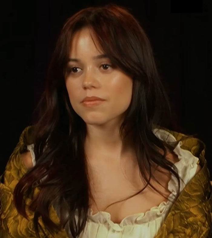 Young woman with long, dark hair, wearing a green and white outfit, expressing serious demeanor.