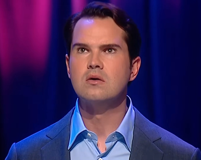 Man in blue shirt and blazer, looking upwards on stage, discussing cosmetic tweakments.