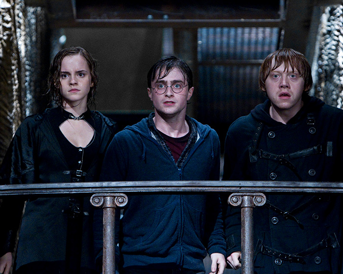 Characters from Harry Potter series look surprised and serious on a set resembling a dark chamber.