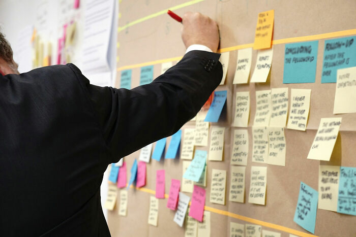 Person in a suit writing on a board filled with colorful sticky notes in an office setting.