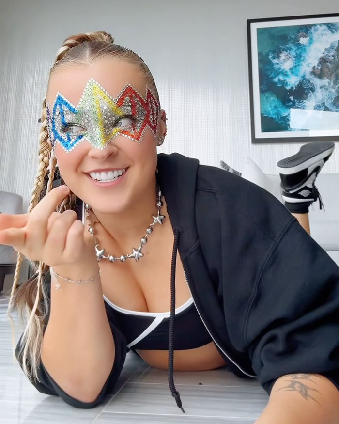 Rainbow mask worn by JoJo Siwa, lying down in sporty outfit with braided hair, debuting a new bold look.