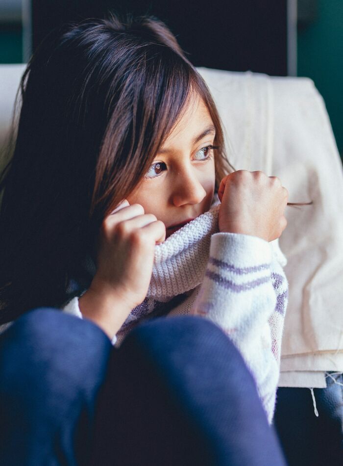 Young girl looking anxious, wrapped in a sweater, embodying the fear of a true scary story.
