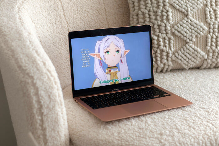 Anime scene on a laptop screen, featuring an elf character with subtitles, set on a textured couch.