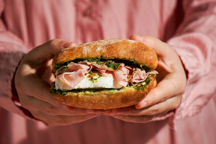 Person holding gourmet sandwich, representing a 'lifetime supply' of deli delights, in a casual setting.