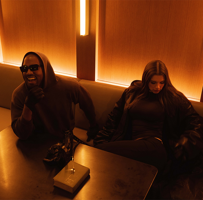 Two individuals seated in a dimly lit room wearing dark clothing.
