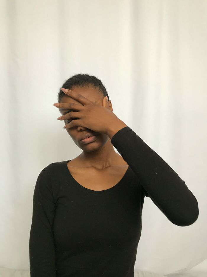 Person in black shirt covering face with hand, conveying judgmental expression.