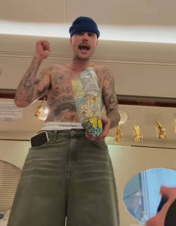Shirtless man with tattoos, wearing a beanie, holds a colorful bag in a casual setting, addressing impostor syndrome concerns.