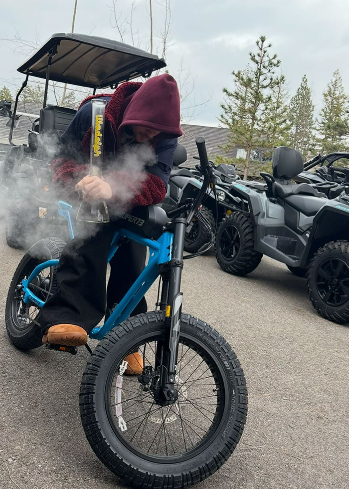 Person in a red hoodie on a blue electric bike, with smoke in the background.