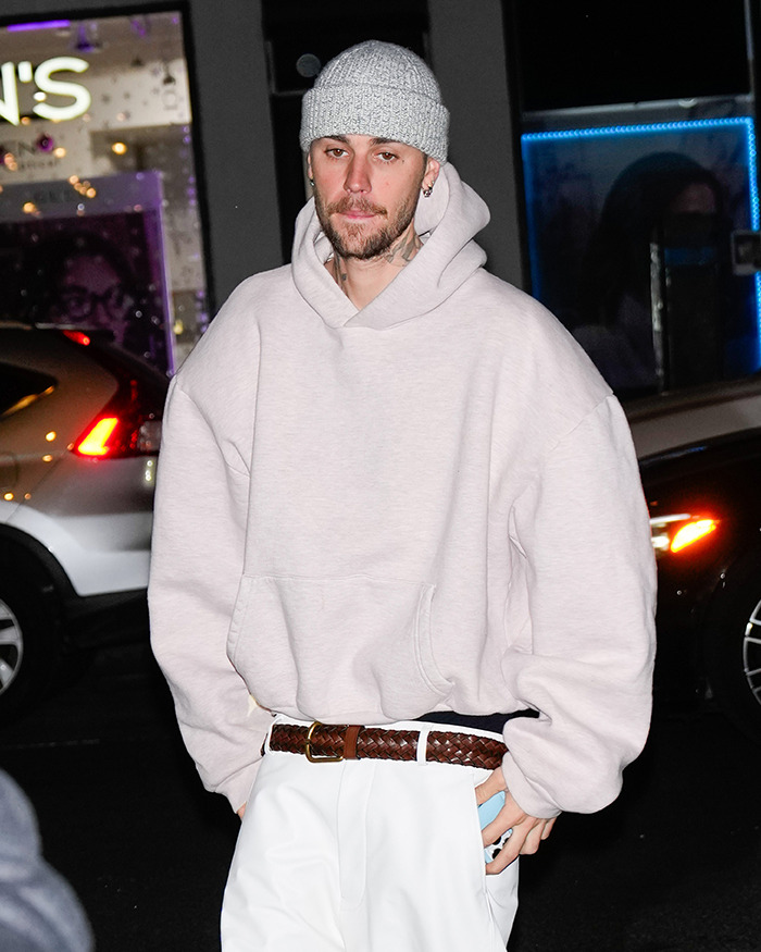 Justin Bieber in a gray beanie and hoodie walking at night.