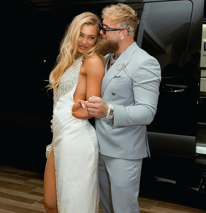 Man in a suit embraces woman in an elegant dress, posing in front of a vehicle at night, linked to "World's Hottest Speed Skater".