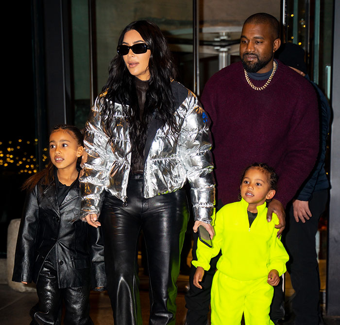 Kim Kardashian and Kanye walking with their children in stylish outfits.