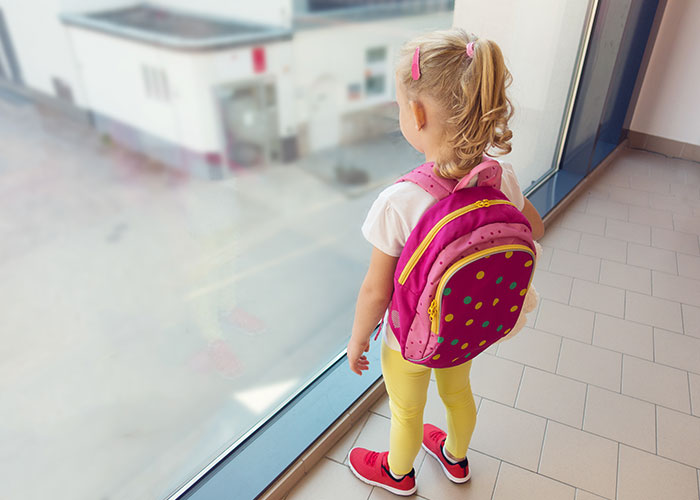 Child with a pink backpack looking out a window, linked to neighbor conflict over childcare.