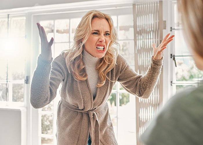 Upset woman gesturing angrily inside a bright room, expressing frustration towards her neighbor.