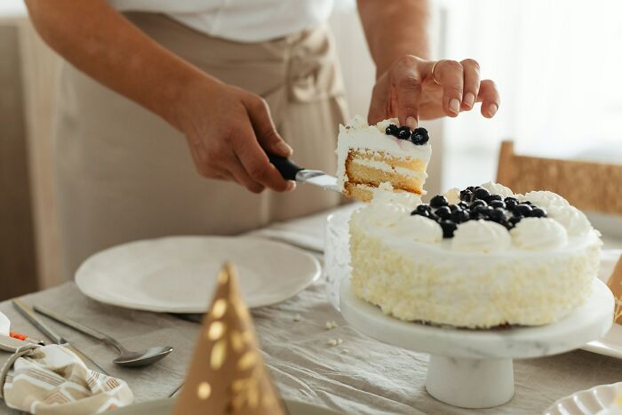Person slicing a cake topped with blueberries on a table, depicting a disappointing job bonus scenario.