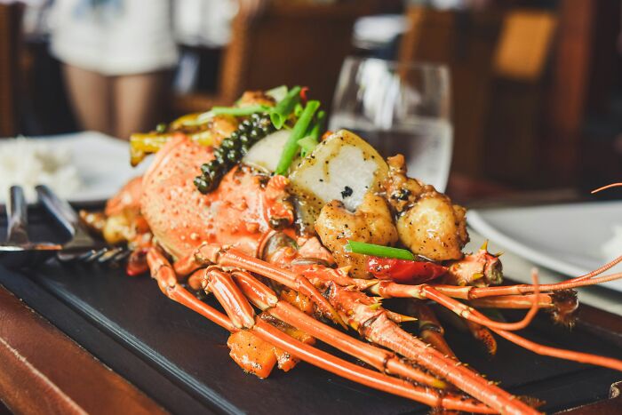 A gourmet seafood dish featuring lobster and vegetables garnished with herbs on a wooden platter, often considered disgusting by some.