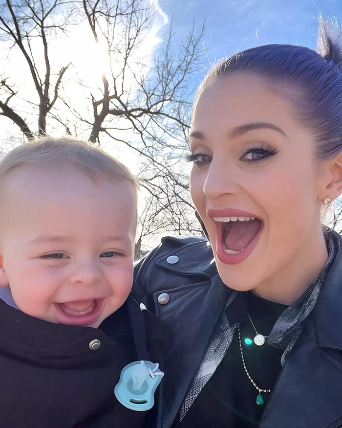 Kelly Osbourne wearing a black leather jacket, holding a baby in winter attire.