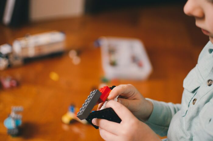Child playing with Lego bricks, potential weird object doctors removed, wearing a light blue shirt at a wooden table.