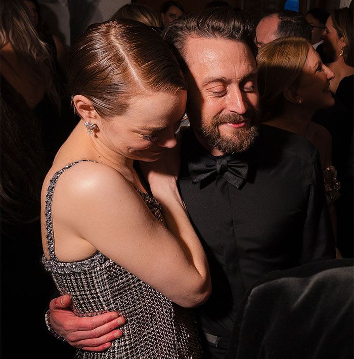 Two people sharing a hug in formal attire at an Oscars 2025 event, capturing a candid behind-the-scenes moment.