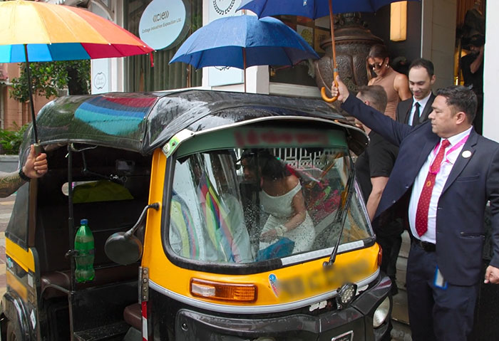 A bride and groom sit in a decorated rickshaw as people hold umbrellas, highlighting cultural contrasts with Disney's Aladdin.