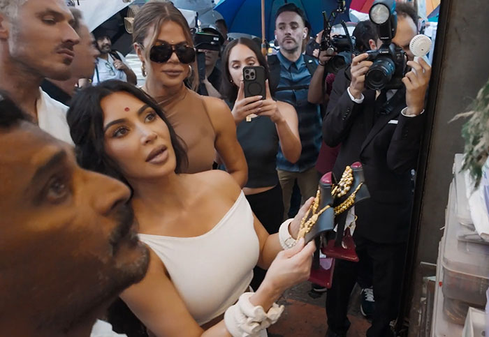 Kim Kardashian holds sandals in a busy market, photographers capturing the moment.