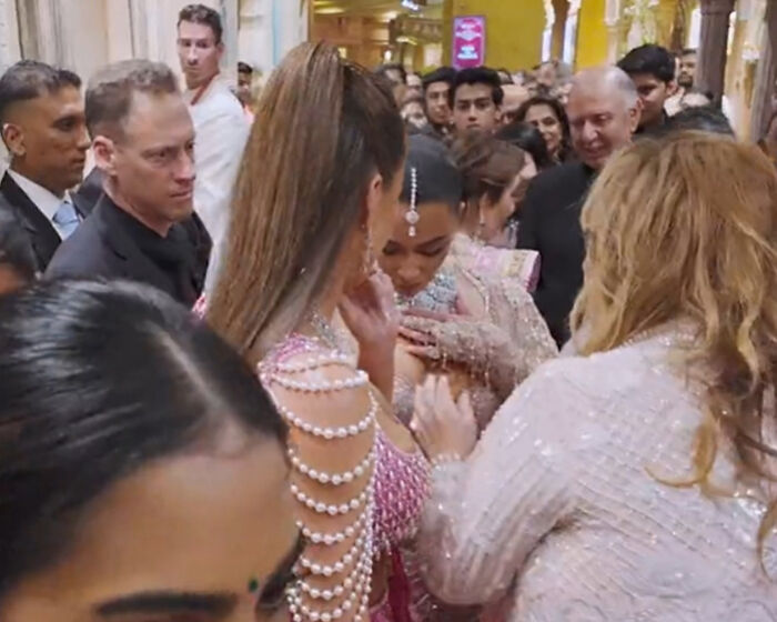 Group surrounding a woman in a crowded event, dressed in glamorous outfits, with a focus on discussion and attention.