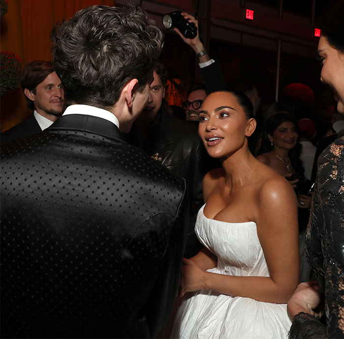 Person in black jacket talks to woman in white dress at Oscars 2025.