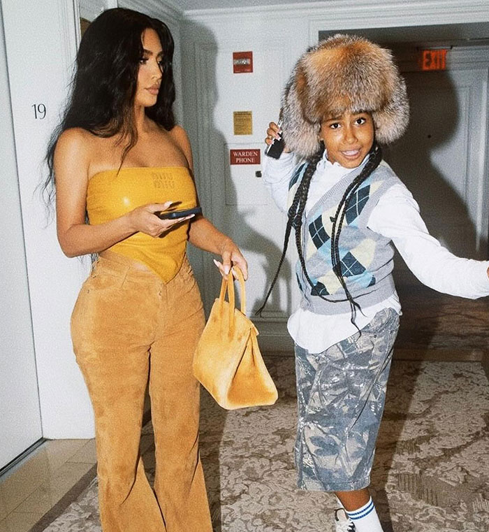 Woman in a yellow top and child in hat, indoors. They appear to be having a cheerful interaction.