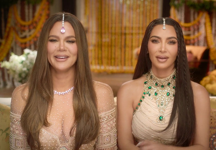 Kim Kardashian and another person wearing traditional Indian jewelry in a lavishly decorated setting.