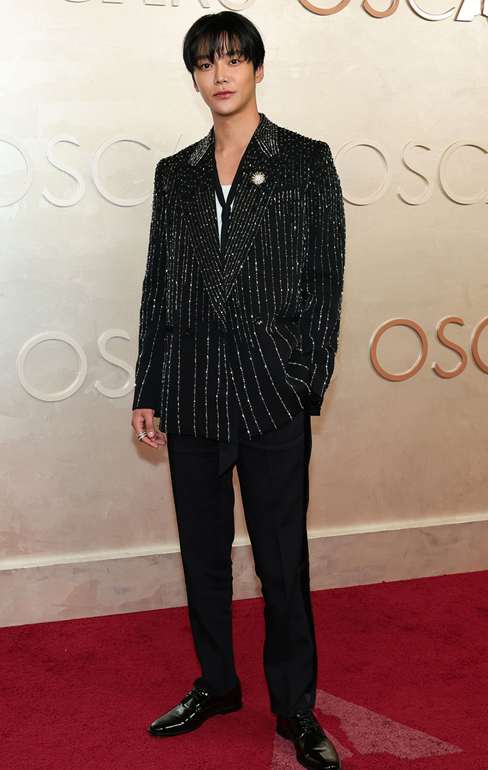Celebrity poses on Oscars red carpet in black glittering suit, exuding Hollywood glamor and style.
