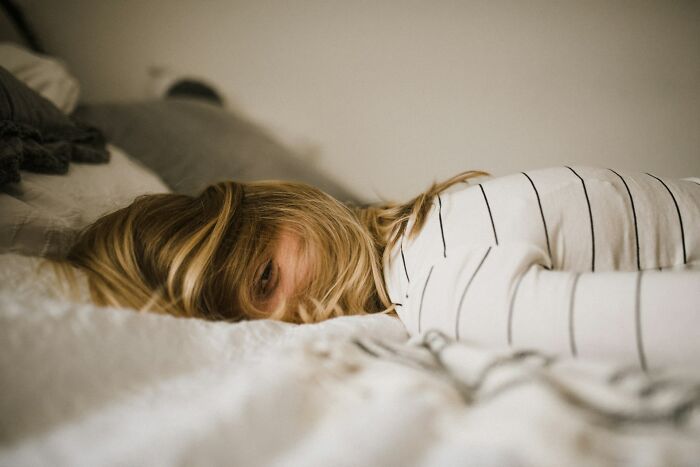 Person lying face down on a bed, partially covered by blonde hair, in a private setting.
