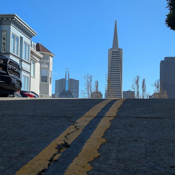 San Francisco skyline captured by Sage Akaboshi, featuring a steep street and iconic Transamerica Pyramid under blue skies.