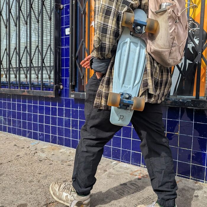 A skateboarder in San Francisco with a blue skateboard and backpack, captured by photographer Sage Akaboshi.