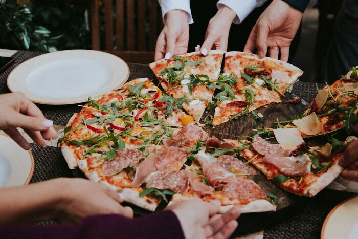 People sharing a large pizza, enjoying their lifetime supply win at an outdoor table setting.