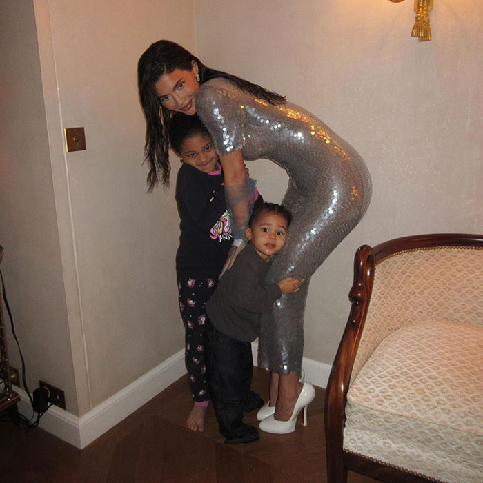 Woman in a sequined dress hugging two children in a cozy room setting.