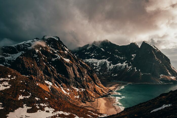 Dramatic coastal landscape with stunning beach, surrounded by rugged mountains under stormy skies.