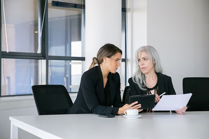 Two women in a serious discussion at a table with documents, highlighting family financial disputes.