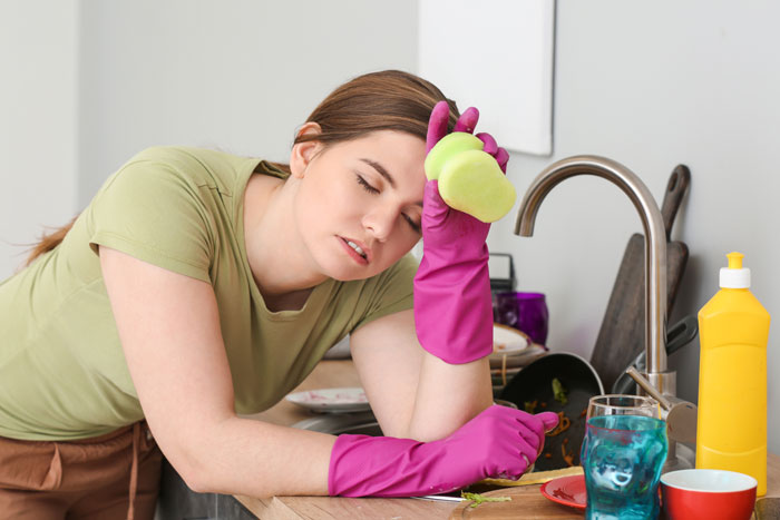 Woman in pink gloves feeling exhausted in kitchen, symbolizes issues with a lazy boyfriend.