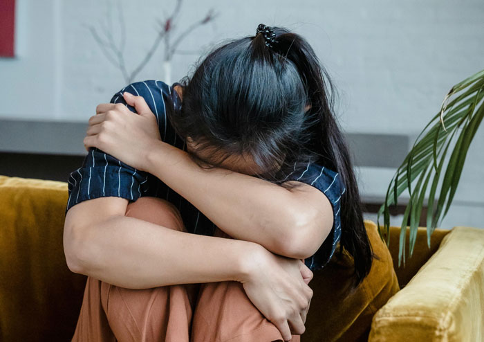 Woman with head down, hugging knees on a sofa, reflecting on boyfriend's laziness and lectures about her son.