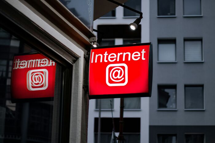 Red "Internet" sign with an @ symbol on a city street reflecting in a nearby window, representing historical turning points.