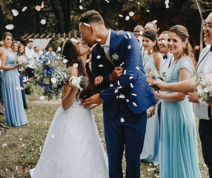 Wedding couple kissing surrounded by friends in blue dresses, capturing friendship and celebration.
